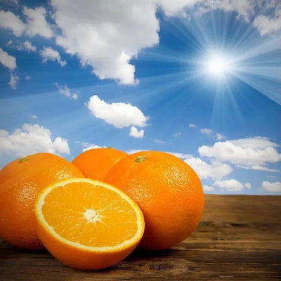 Whole and halved oranges on wood under bright sun, blue sky