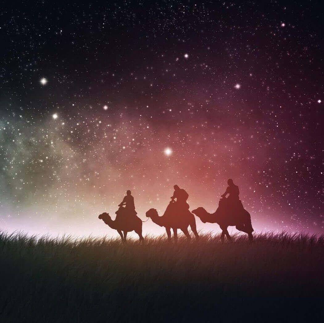 Three silhouetted camels with riders against a starlit night sky showing the Milky Way.