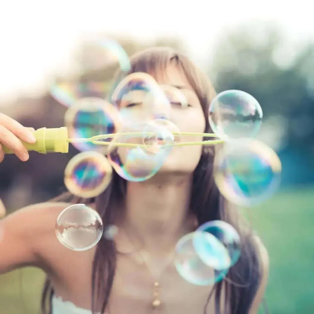 Young woman blowing bubbles outdoors, surrounded by a dreamy blur of colorful soap bubbles.