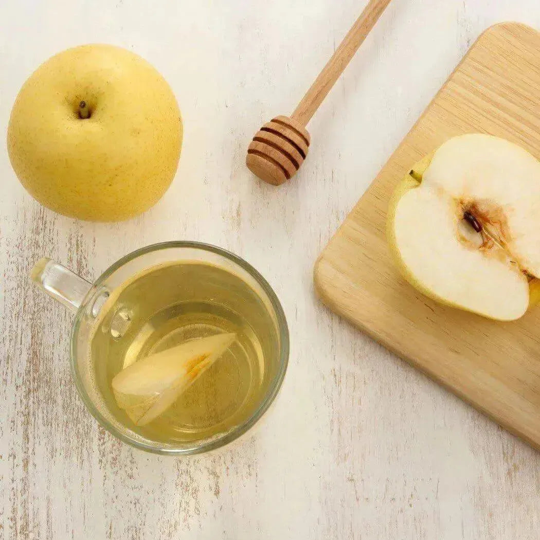 Whole yellow pear beside sliced one on wooden board with honey dipper for White Tea + Pear Fragrance Blend